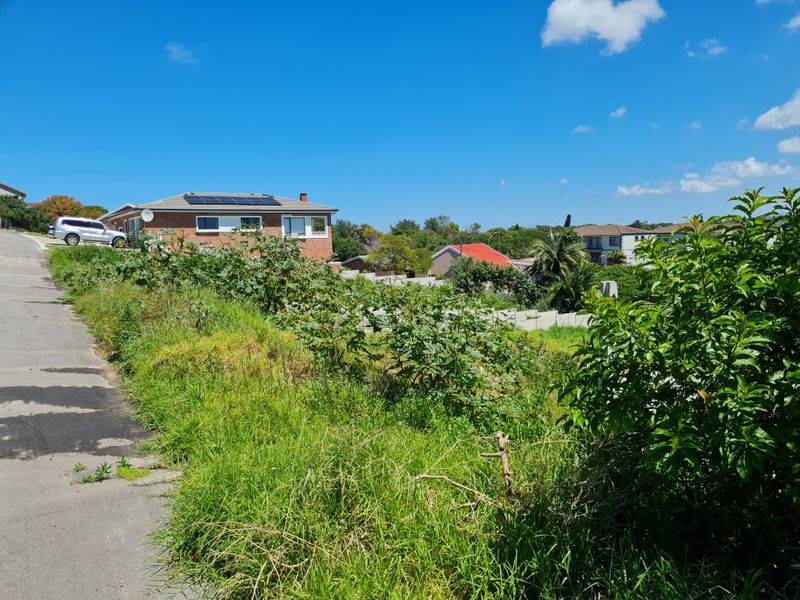 A vacant residential plot featuring sloped terrain and direct access to a paved road in an established neighborhood setting.