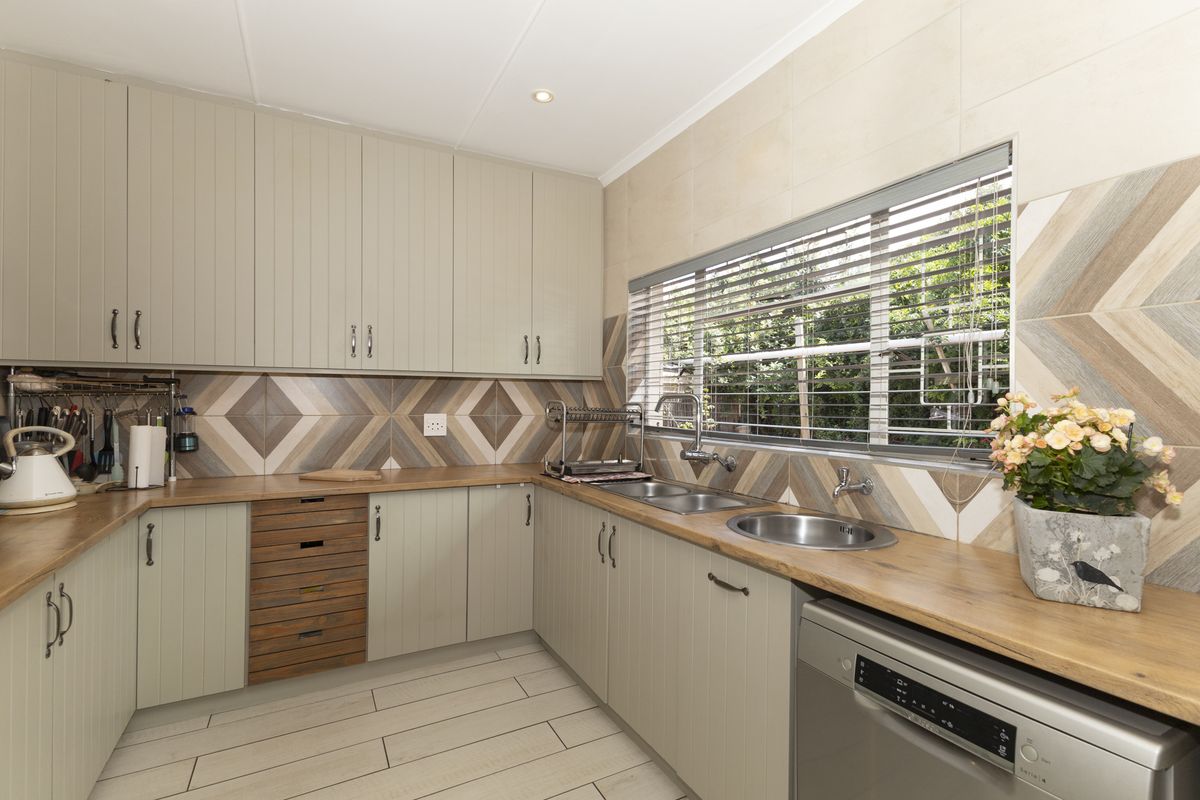 A well-maintained kitchen featuring light-toned cabinetry, wooden countertops, a double stainless steel sink, and decorative tiled backsplash with integrated dishwasher.