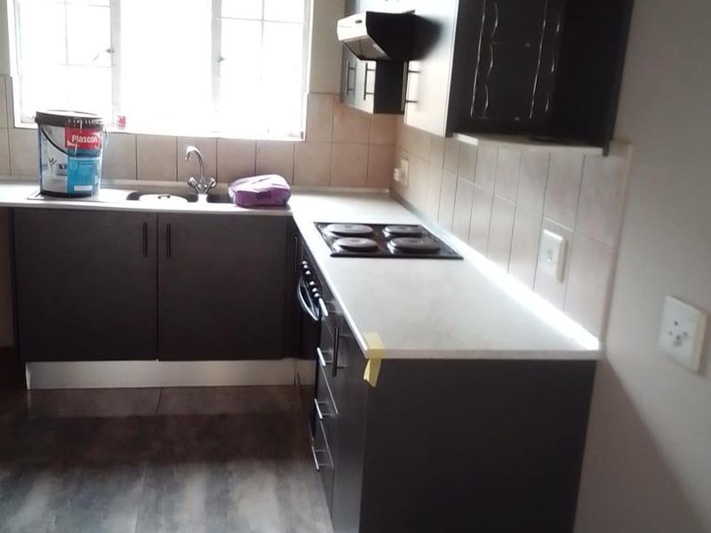 A compact kitchen featuring dark cabinetry, light countertops, an electric hob with extractor fan, and tiled flooring.