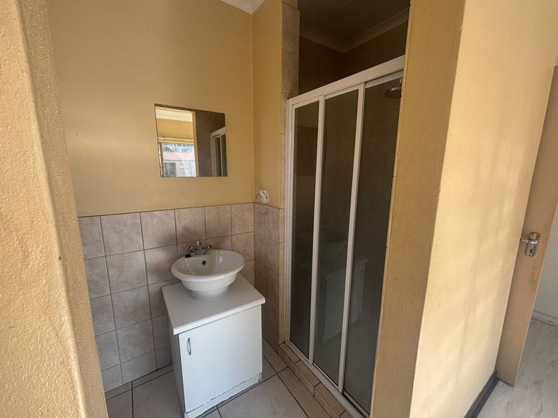 A compact bathroom featuring a vanity basin and a glass-enclosed shower, requiring cosmetic updates to modernize the space.