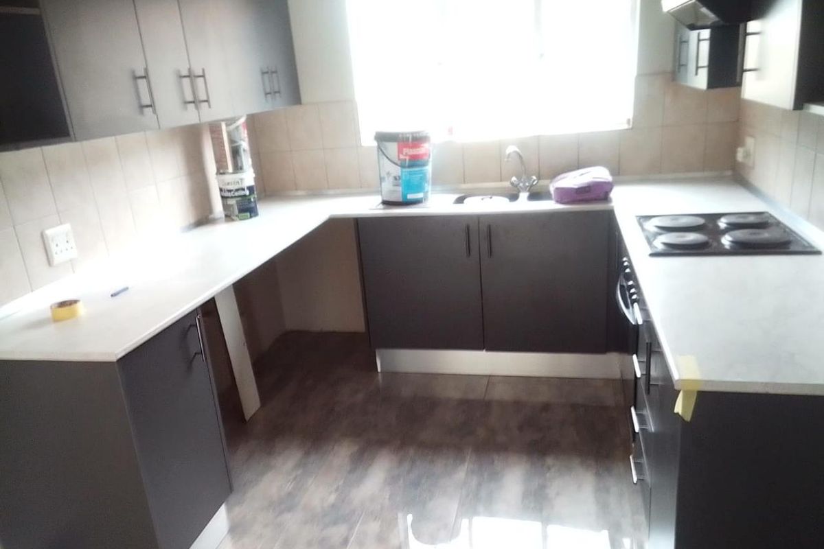 A functional kitchen featuring dark cabinetry, light countertops, an electric hob, and an extractor fan, with tiled splashbacks and wood-look flooring.