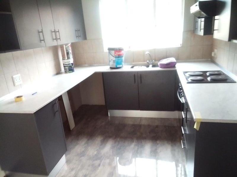 A functional kitchen featuring dark cabinetry, light countertops, an electric hob, and an extractor fan, with tiled splashbacks and wood-look flooring.