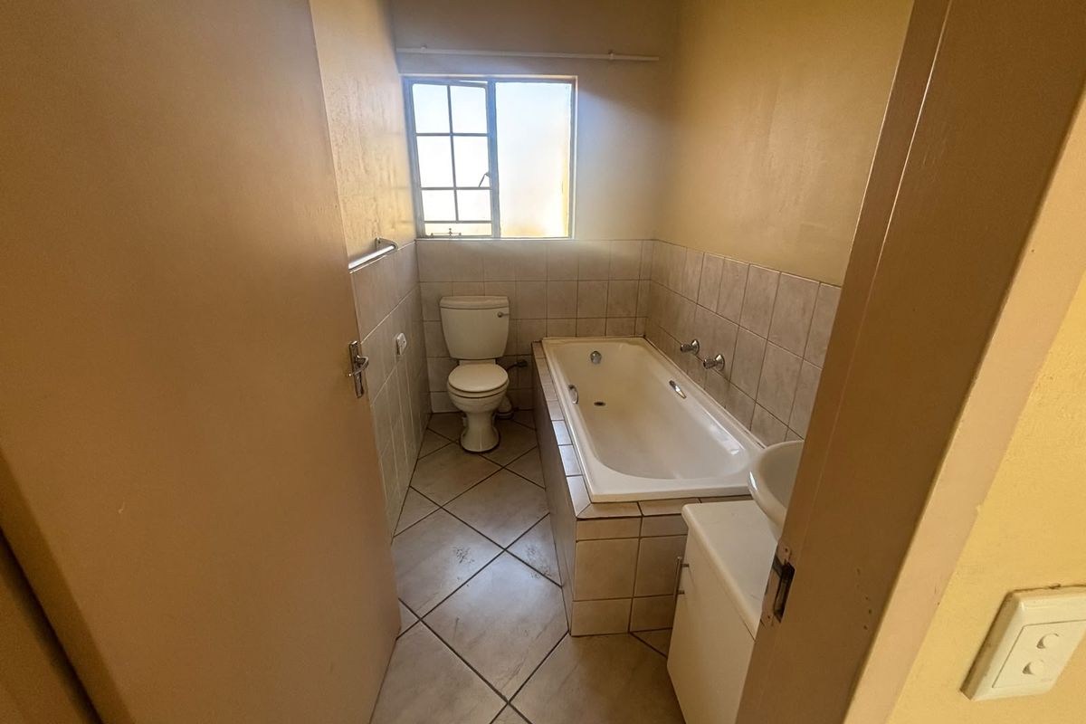 A functional bathroom featuring a built-in bathtub, toilet, and tiled finishes, offering a blank canvas for potential modernization and renovation.