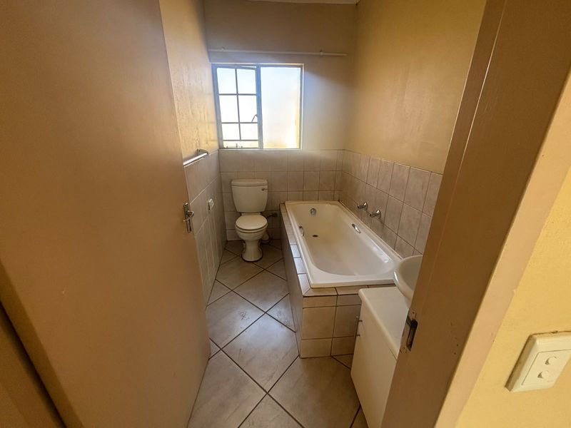 A functional bathroom featuring a built-in bathtub, toilet, and tiled finishes, offering a blank canvas for potential modernization and renovation.