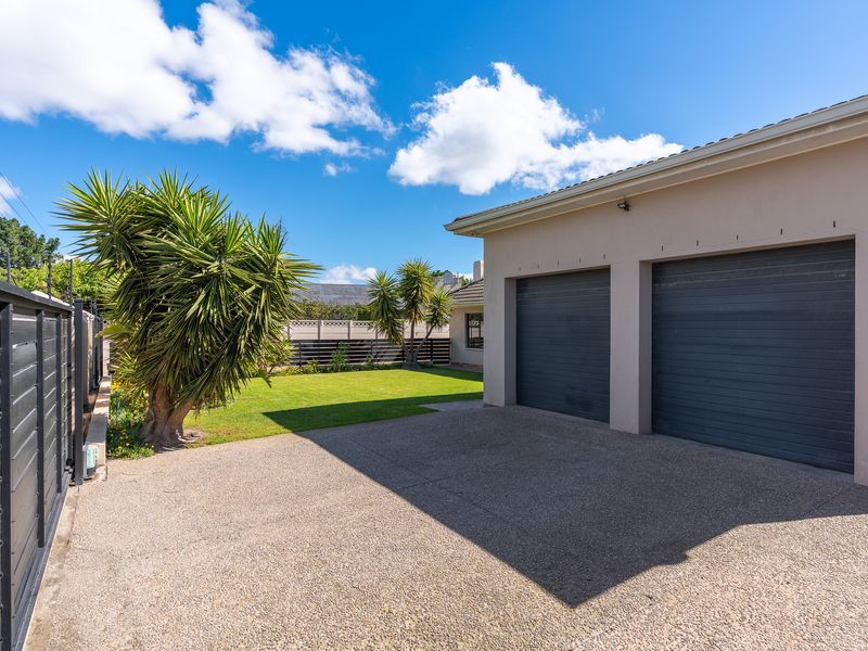 A well-maintained exterior view featuring a double garage with dark roller doors, an exposed aggregate driveway, and a neat lawn area.