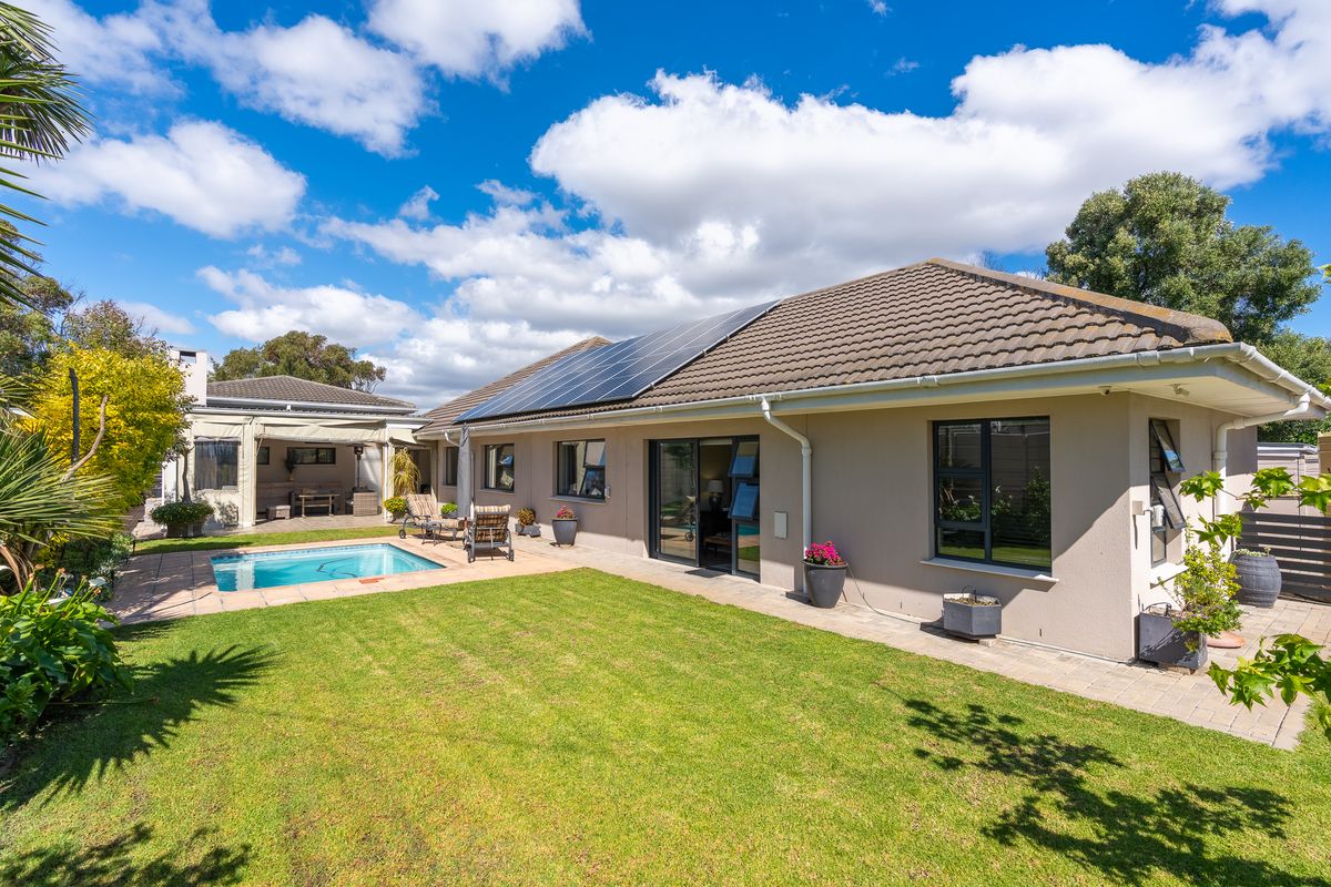 Rear view of the property featuring a well-maintained lawn, a swimming pool, paved patio area, and solar panels installed on the tiled roof.