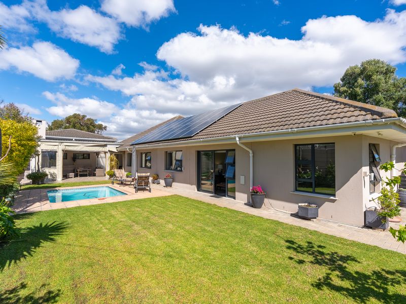 Rear view of the property featuring a well-maintained lawn, a swimming pool, paved patio area, and solar panels installed on the tiled roof.