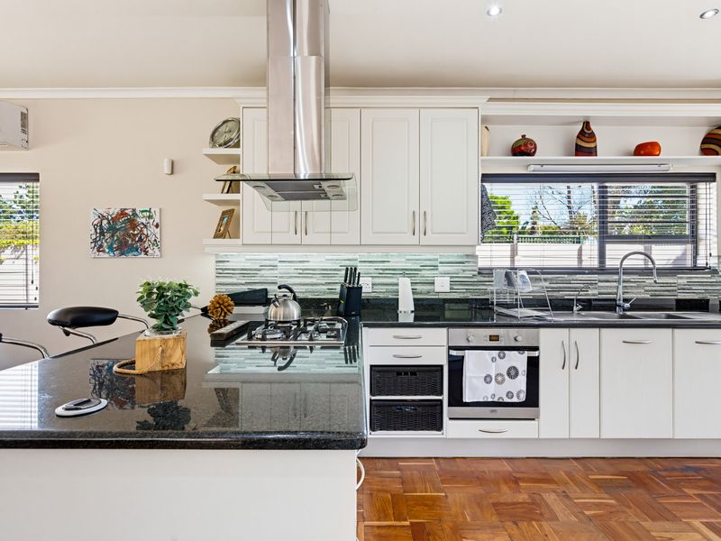 Modern kitchen featuring granite countertops, a gas hob with stainless steel extractor, built-in oven, and elegant parquet flooring.