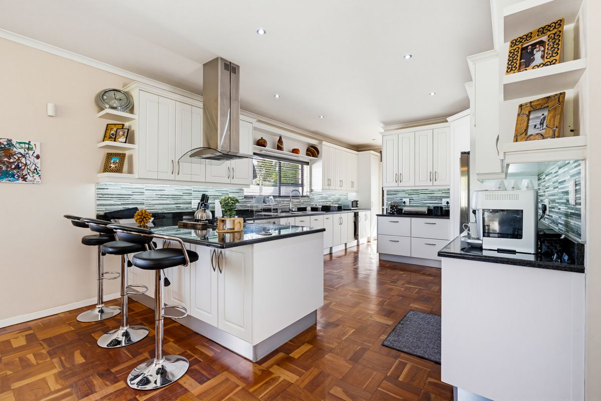 A well-appointed kitchen featuring white cabinetry, dark stone countertops, a central island with breakfast bar, and elegant parquet flooring.