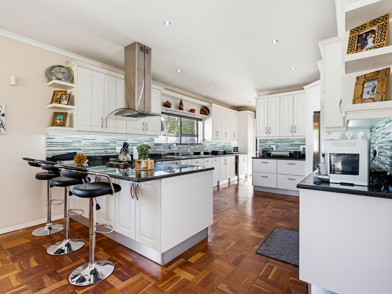 A well-appointed kitchen featuring white cabinetry, dark stone countertops, a central island with breakfast bar, and elegant parquet flooring.