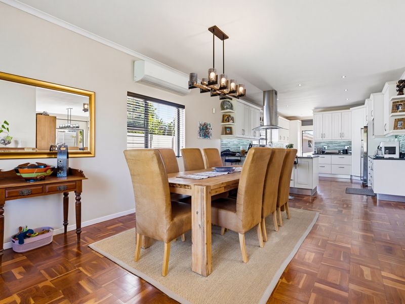 Spacious open-plan dining and kitchen area featuring warm parquet flooring, modern white cabinetry, a central kitchen island, and elegant pendant lighting.