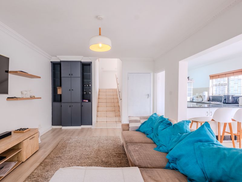 An open-plan living area featuring laminate flooring, crown molding, built-in storage cabinetry, and a staircase, with an adjacent kitchen breakfast bar.