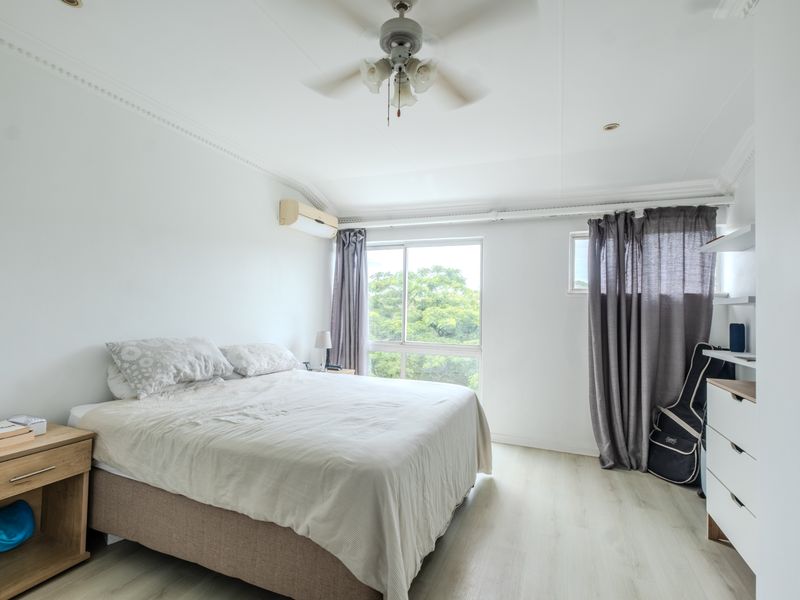 A bright bedroom featuring laminate flooring, a ceiling fan, a split-system air conditioner, and built-in wardrobe storage.