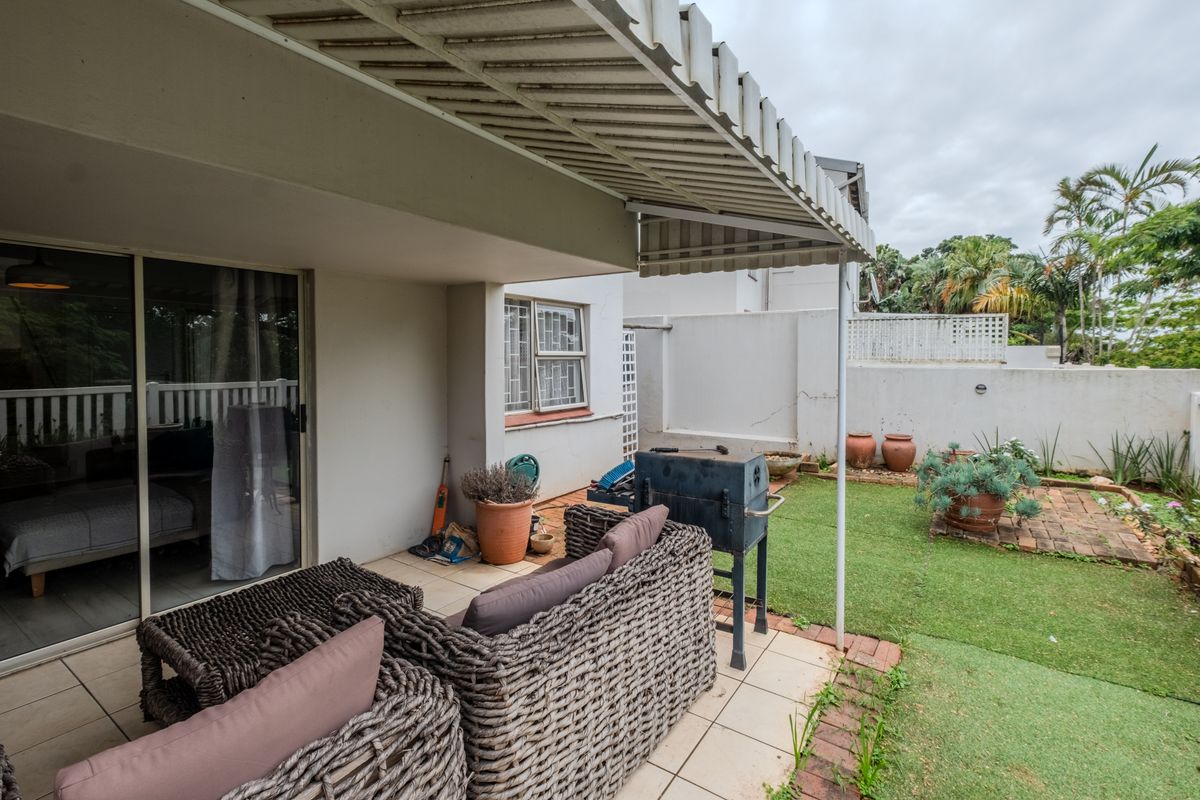 Covered patio area featuring tiled flooring, a retractable awning, and direct access to a small private garden with brick edging and boundary walls.