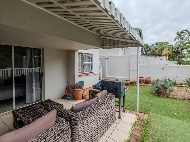 Covered patio area featuring tiled flooring, a retractable awning, and direct access to a small private garden with brick edging and boundary walls.