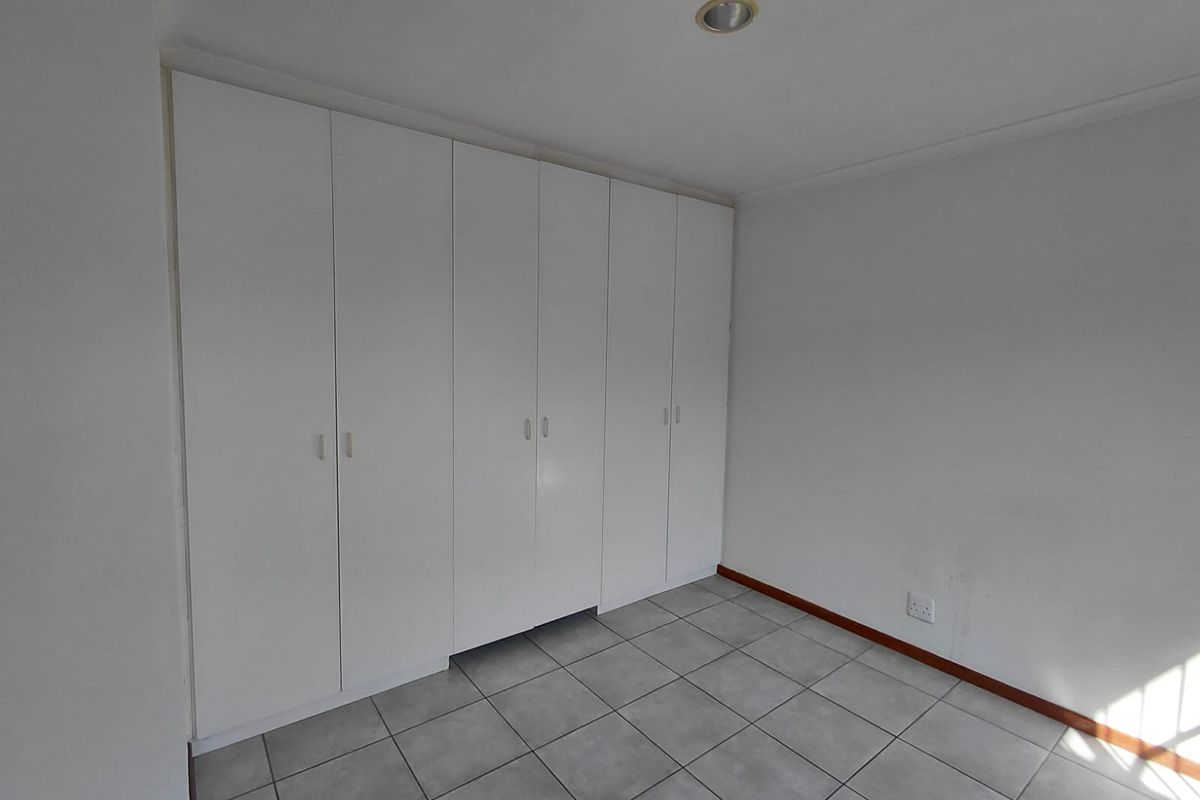 A clean, empty bedroom featuring neutral tiled flooring and extensive white built-in cupboards, offering a versatile space ready for personalization.