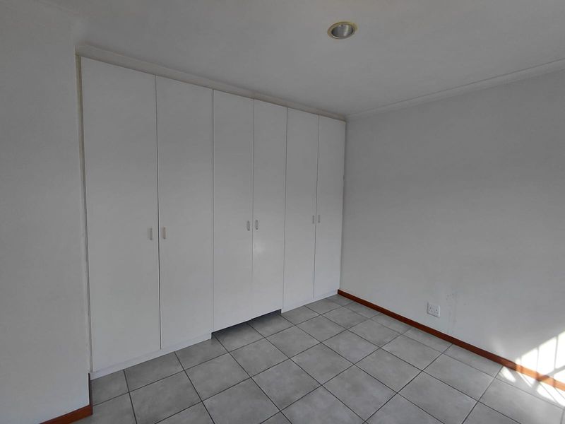 A clean, empty bedroom featuring neutral tiled flooring and extensive white built-in cupboards, offering a versatile space ready for personalization.