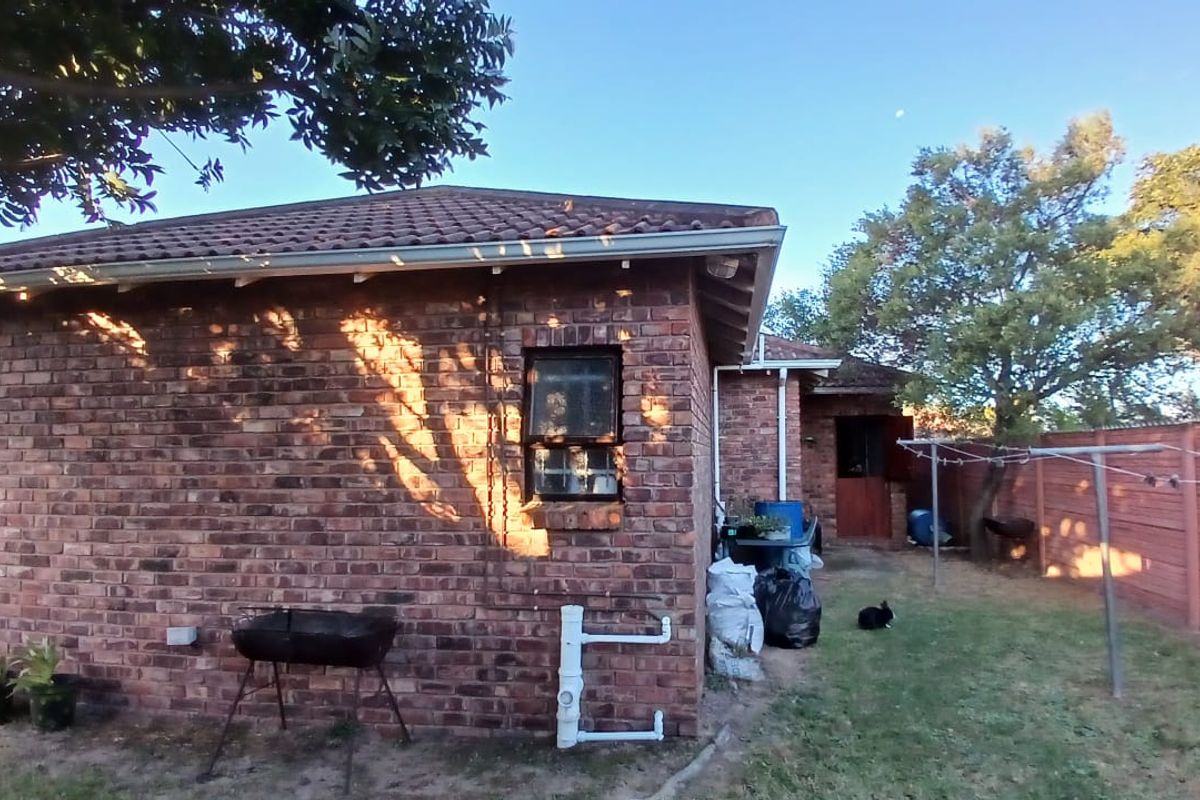 Rear view of a face brick house featuring a tiled roof, steel window frames, and an open garden area with perimeter fencing.