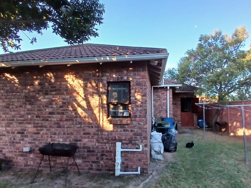 Rear view of a face brick house featuring a tiled roof, steel window frames, and an open garden area with perimeter fencing.