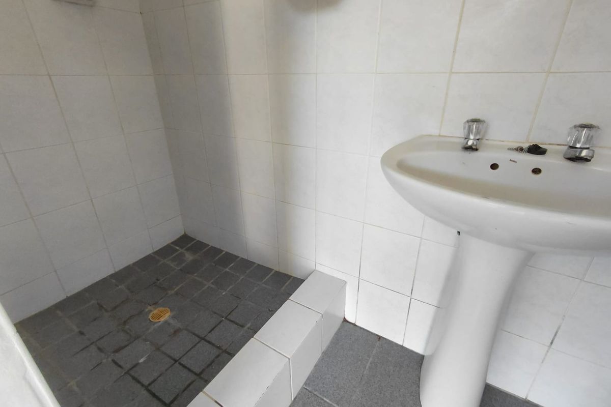 A functional bathroom featuring a pedestal basin and a tiled shower area, requiring cosmetic updates to improve its overall condition and appeal.
