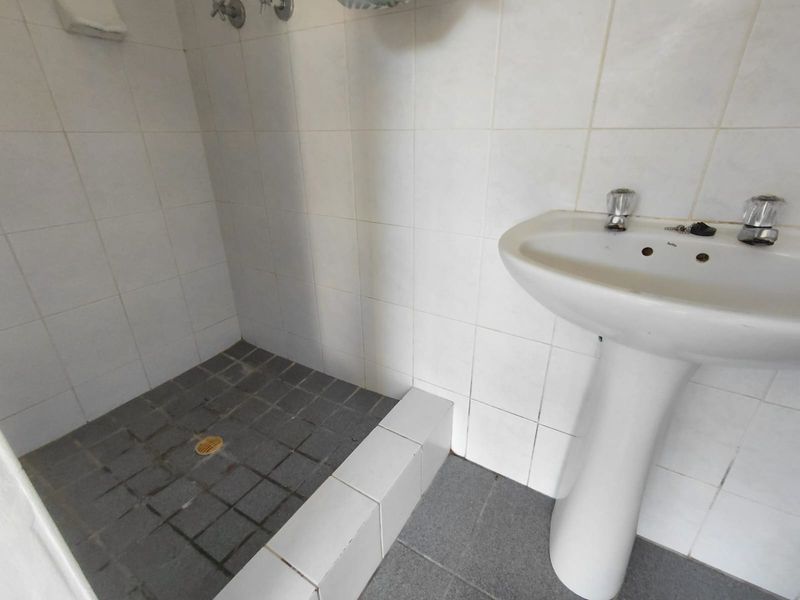A functional bathroom featuring a pedestal basin and a tiled shower area, requiring cosmetic updates to improve its overall condition and appeal.