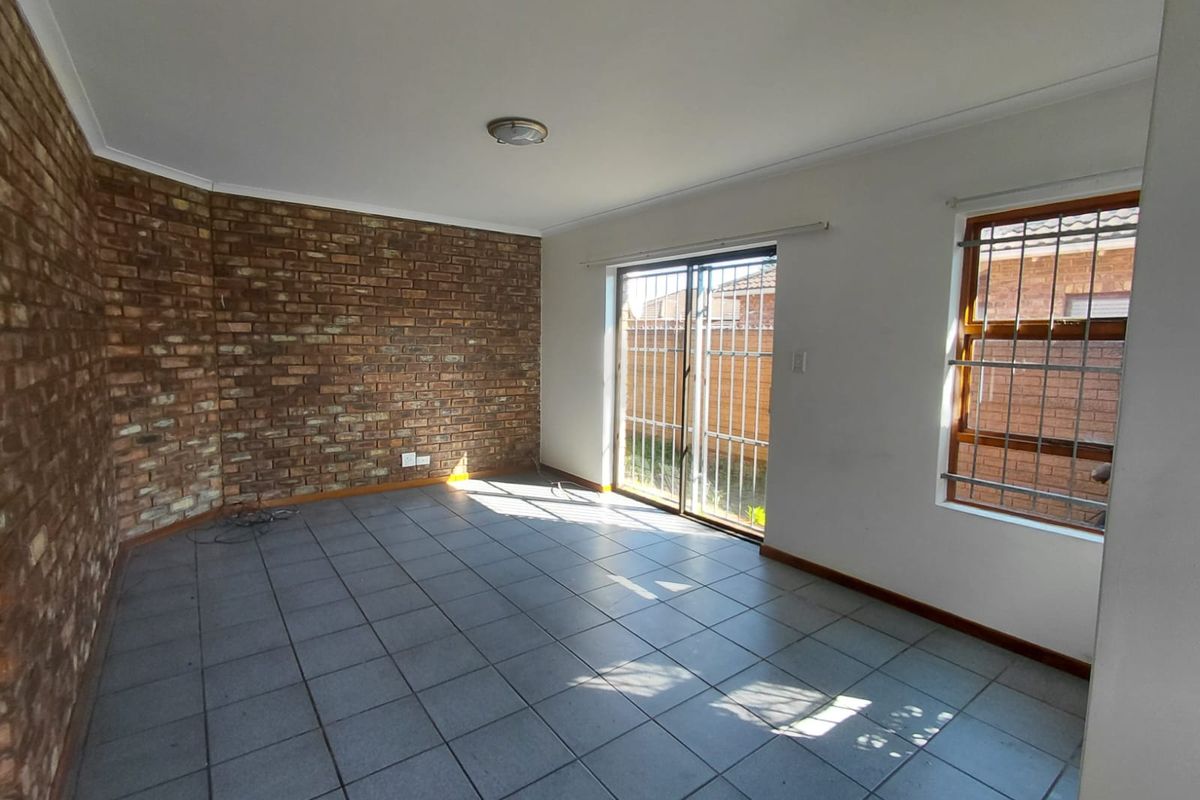 An empty living room featuring an exposed brick wall, tiled flooring, and a sliding glass door with security bars leading to the exterior.
