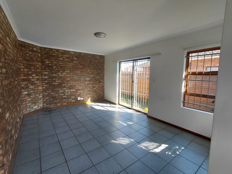 An empty living room featuring an exposed brick wall, tiled flooring, and a sliding glass door with security bars leading to the exterior.
