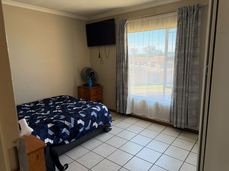 A functional bedroom featuring tiled flooring, a large window for natural light, and built-in storage space.
