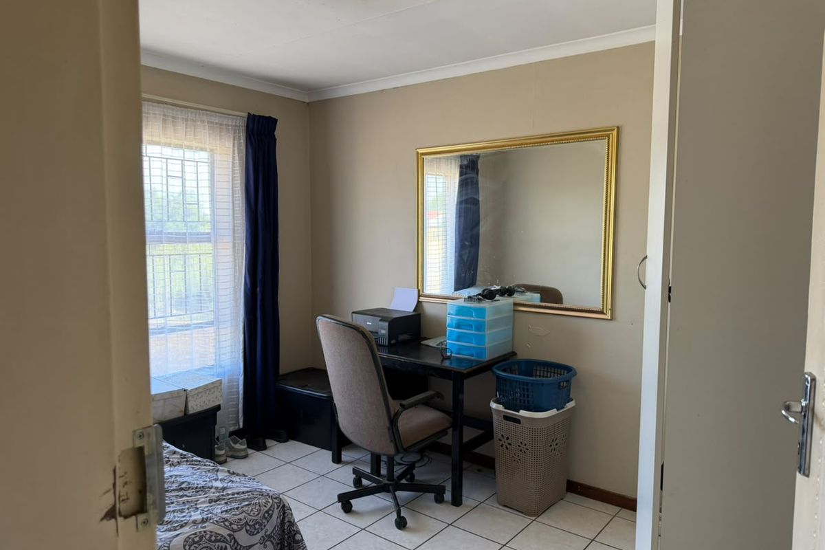 A functional bedroom featuring tiled flooring and a window with security bars, offering a neutral canvas for potential updates.