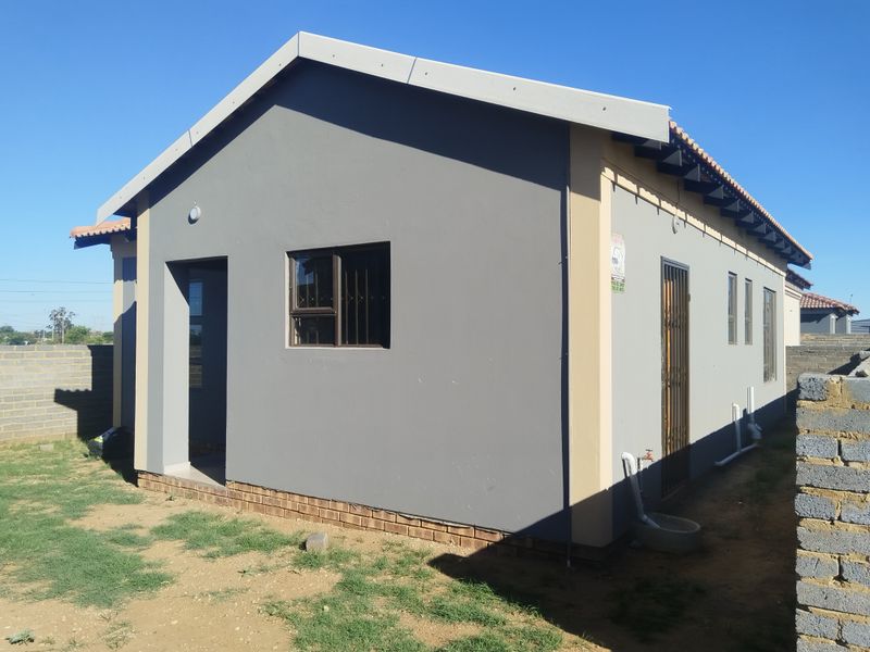 Rear view of a modern single-story house featuring a tiled roof, security gates, and a surrounding brick boundary wall.