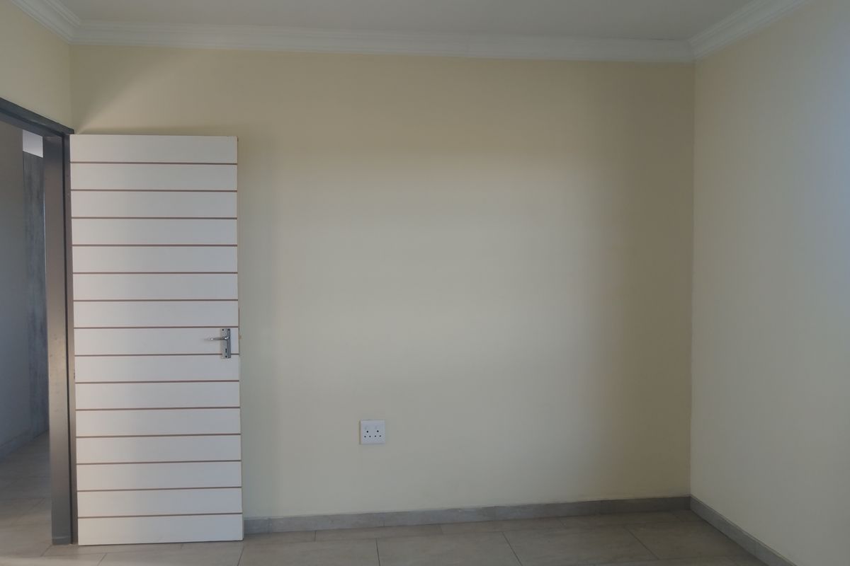 A clean, empty bedroom featuring neutral walls, tiled flooring, and a modern horizontal slatted door, providing a blank canvas for personalization.