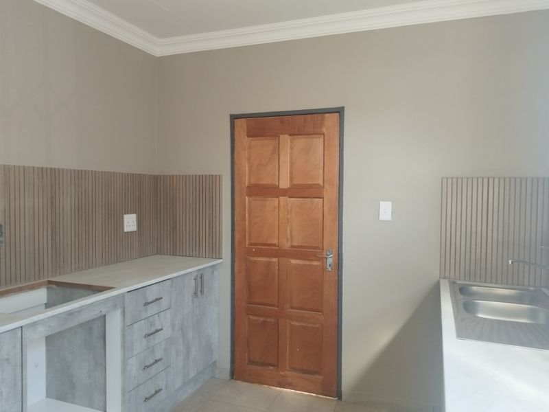 A clean, modern kitchen area featuring grey cabinetry, light-toned laminate countertops, a double bowl sink, and decorative timber wall paneling.