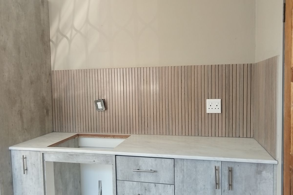 A modern kitchen workspace featuring concrete-look cabinetry, a marble-effect countertop, and a decorative slatted splashback, currently awaiting sink installation.