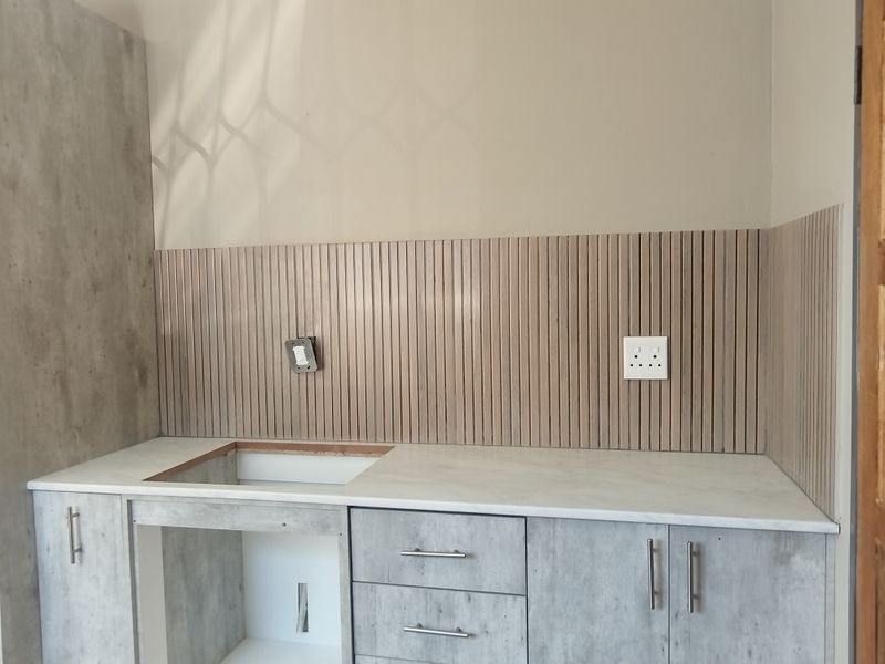 A modern kitchen workspace featuring concrete-look cabinetry, a marble-effect countertop, and a decorative slatted splashback, currently awaiting sink installation.