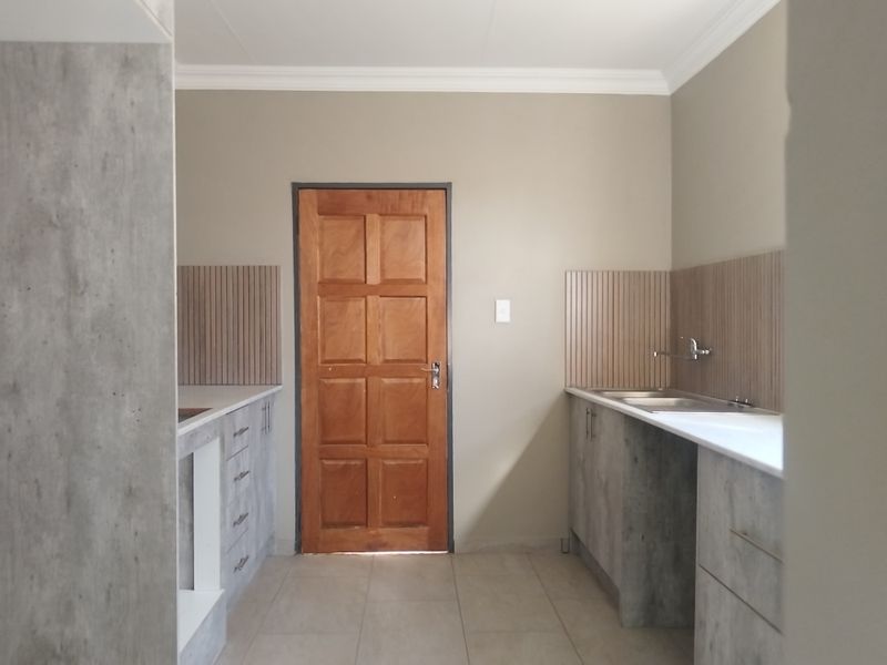 A clean, functional scullery featuring modern grey cabinetry, stainless steel sink, and timber door, providing ample prep and wash-up space.