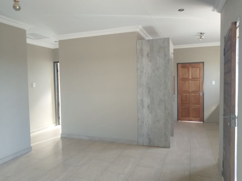 An open-plan living area featuring neutral wall tones, modern tiled flooring, and clean architectural lines, providing a versatile space ready for interior design.