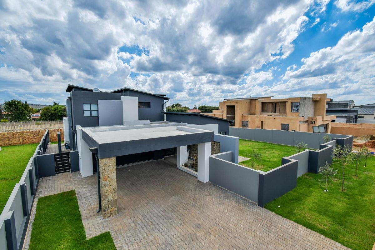 Aerial view of a modern double-story residence featuring a paved driveway, covered carport, stone-clad pillar, and landscaped garden with perimeter walling.