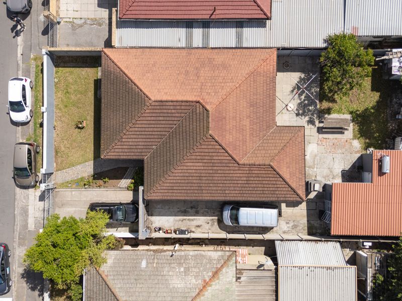 Aerial view of the property showing the roof structure, paved driveway, boundary walls, and surrounding garden area.