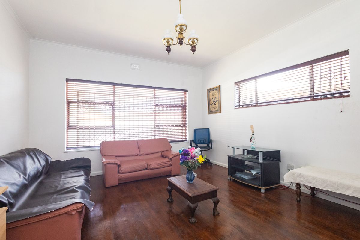 A spacious living room featuring polished timber flooring, large windows with venetian blinds, and classic ceiling detailing.