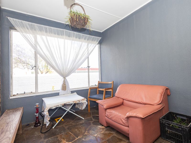 A sunroom or enclosed patio area featuring stone flooring and large windows, providing a bright space with potential for modernization.