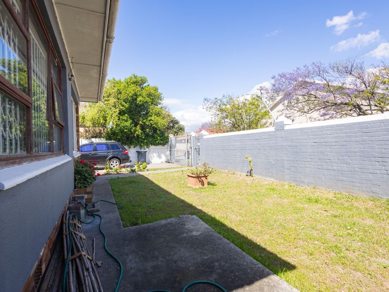 A rear garden area featuring a lawn, concrete pathway, and a painted perimeter brick wall with a metal access gate.