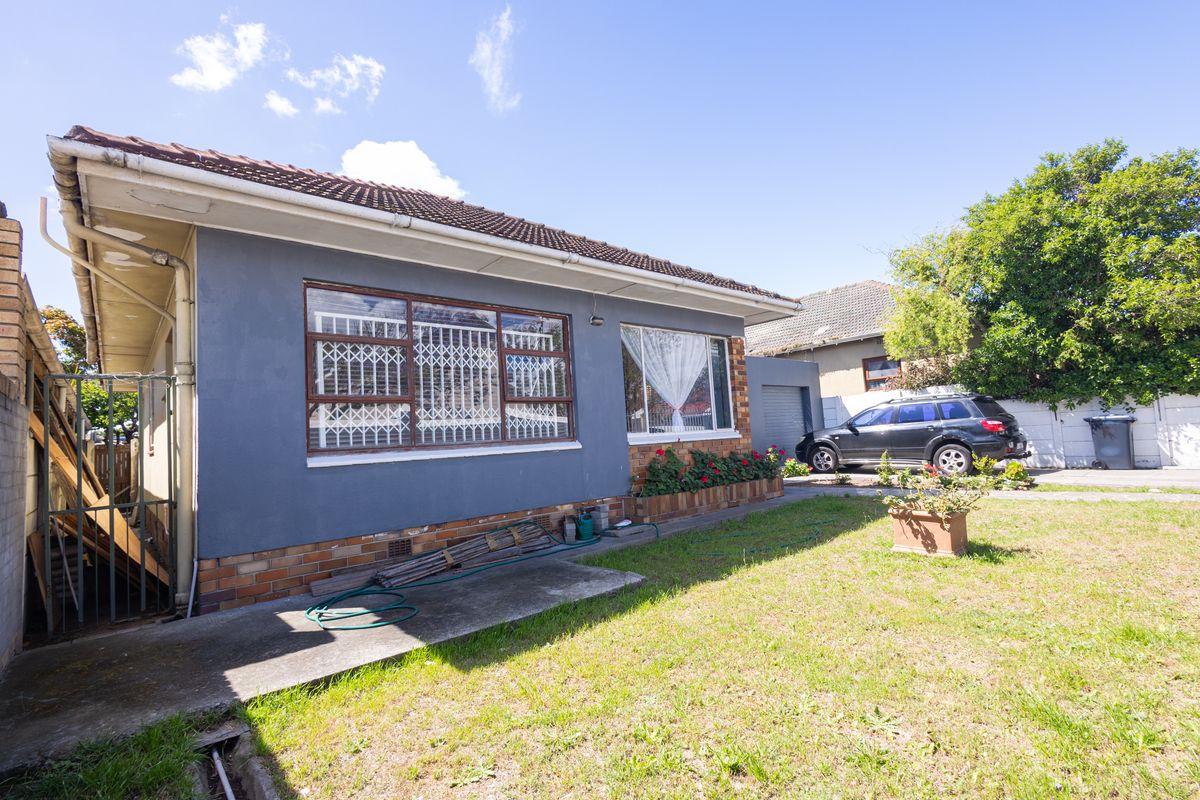 Rear view of the property featuring a brick and rendered facade, tiled roof, security window bars, and a concrete pathway leading to the garden area.