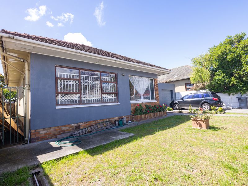 Rear view of the property featuring a brick and rendered facade, tiled roof, security window bars, and a concrete pathway leading to the garden area.