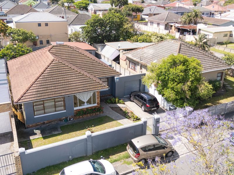 Aerial view of a residential property featuring a tiled roof, enclosed front garden with boundary wall, and a paved driveway leading to a garage.