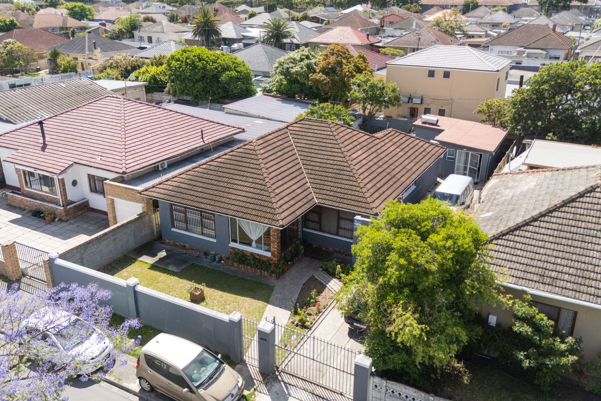 Aerial view of a residential property featuring a tiled roof, front garden, paved driveway, and secure boundary walling in a suburban neighborhood.