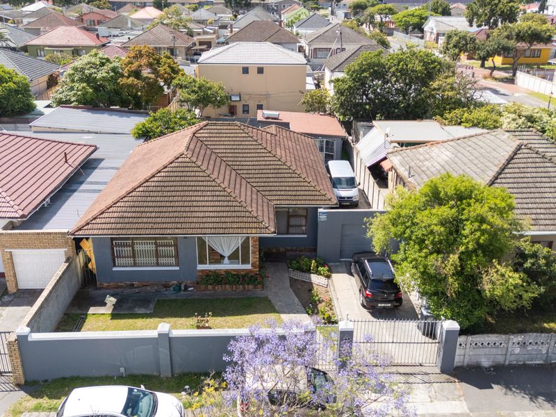 Aerial view of a residential property featuring a tiled roof, paved driveway, and secure boundary wall with gated access in a suburban neighborhood.