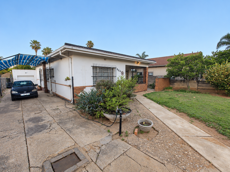 Front view of a single-story house featuring a concrete driveway, security bars on windows, and a manageable garden area.