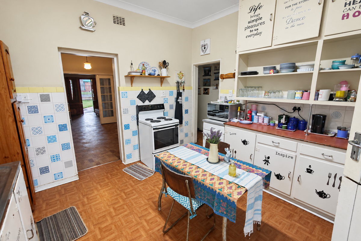 A dated kitchen featuring original cabinetry, open shelving, a freestanding stove, and patterned tiled splashbacks, offering significant potential for a modern renovation.