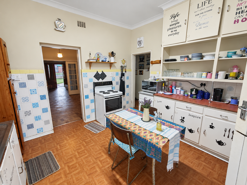 A dated kitchen featuring original cabinetry, open shelving, a freestanding stove, and patterned tiled splashbacks, offering significant potential for a modern renovation.
