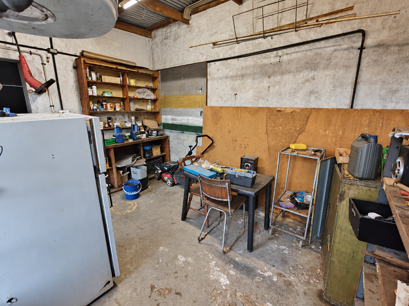 A functional garage space featuring exposed timber rafters, built-in shelving units, and concrete flooring, offering potential for workshop or storage use.